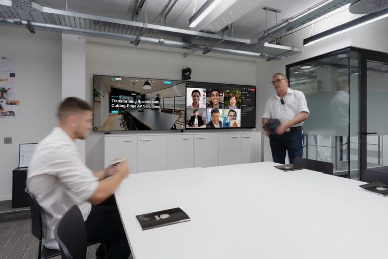 Two people in a meeting room with a Zoom video conference